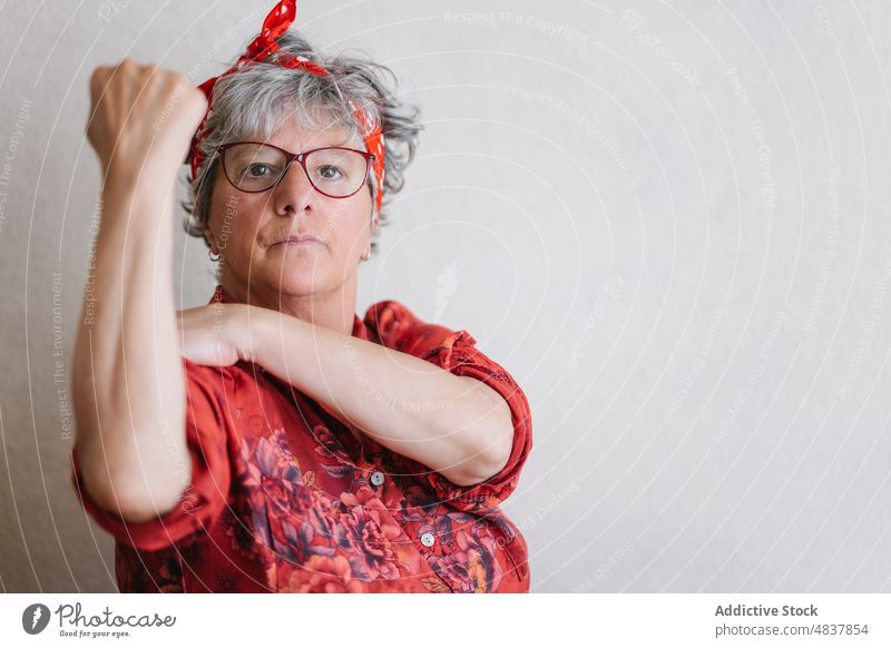 Ernste ältere Feministin zeigt Muskeln und schaut in die Kamera Frau zeigen Bizeps hochstecken Konzentration Stil so tun, als ob Kraft stark manifestieren