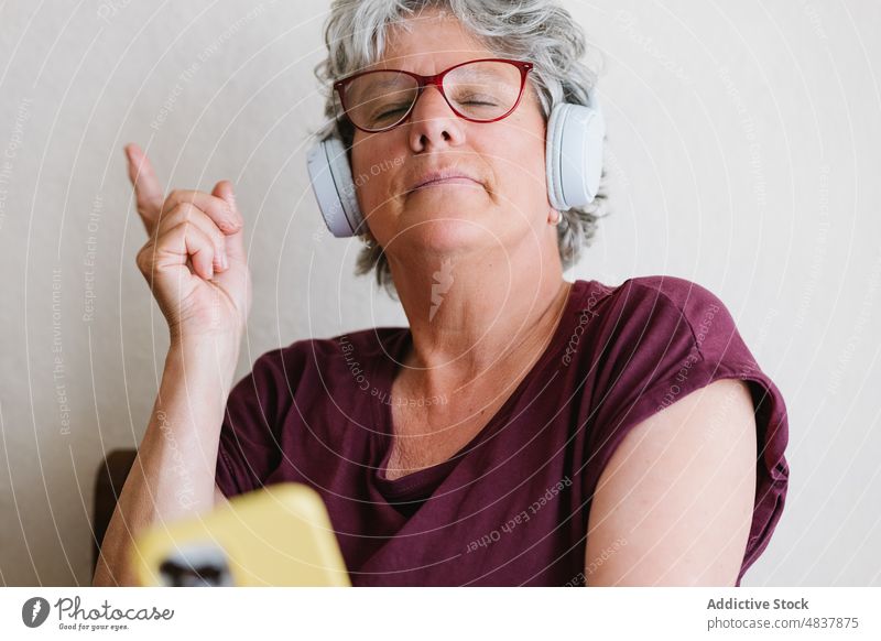 Glückliche reife Frau, die über ihr Smartphone einen Song mit Kopfhörern hört zuhören Musik singen Gesang positiv meloman benutzend Wiedergabeliste