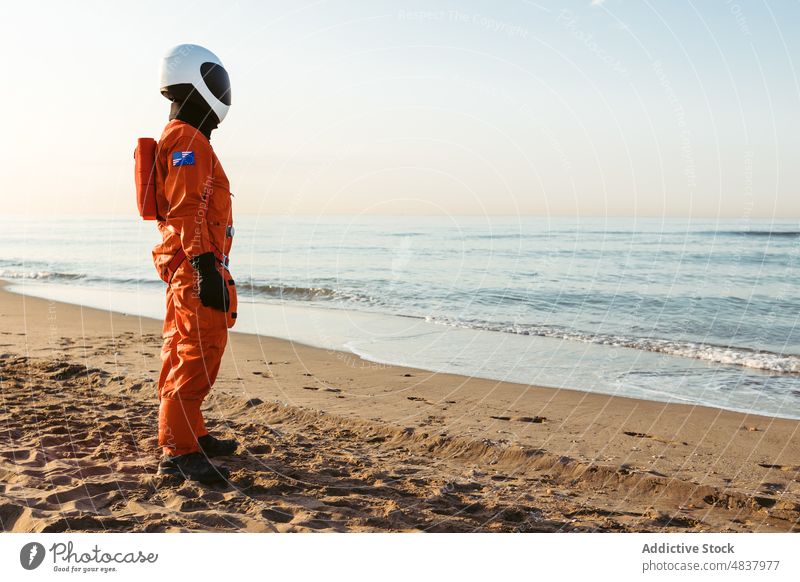 Raumfahrer, der stehend das Meer bewundert Strand MEER Astronaut bewundern Abend ruhen Konzept futuristisch Resort Sand Urlaub Raumanzug Schutzhelm Kosmonaut
