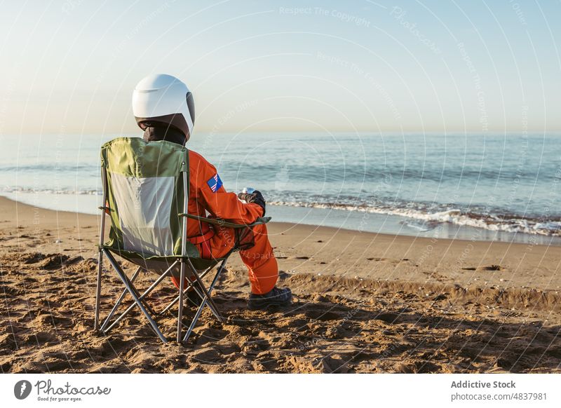 Raumfahrer sitzt auf einem Stuhl und bewundert das Meer Strand MEER Astronaut bewundern Abend ruhen Konzept futuristisch Resort Sand Urlaub Raumanzug Schutzhelm