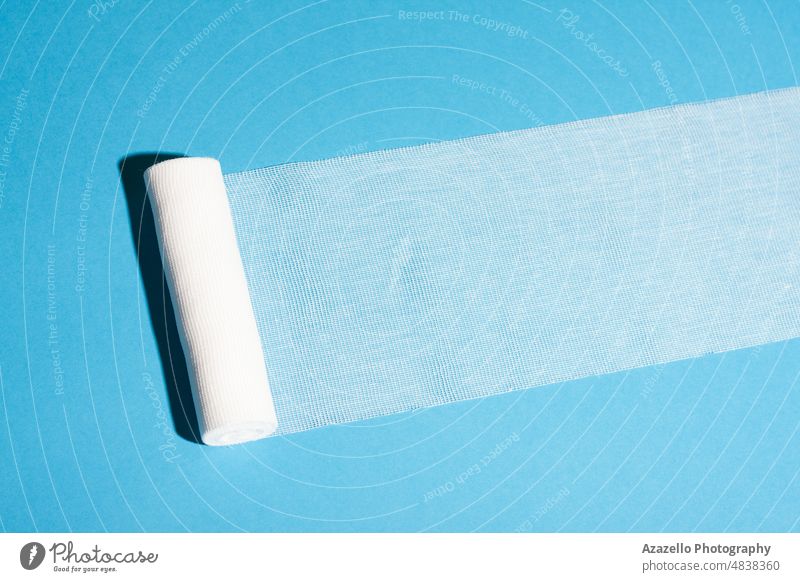 Abgewickelte sterile Verbandrolle auf blauem Hintergrund. Gaze bandagieren Chirurgie Schatten Medizin Unterstützung Verbände Pflege Seihtuch Sauberkeit Stoff