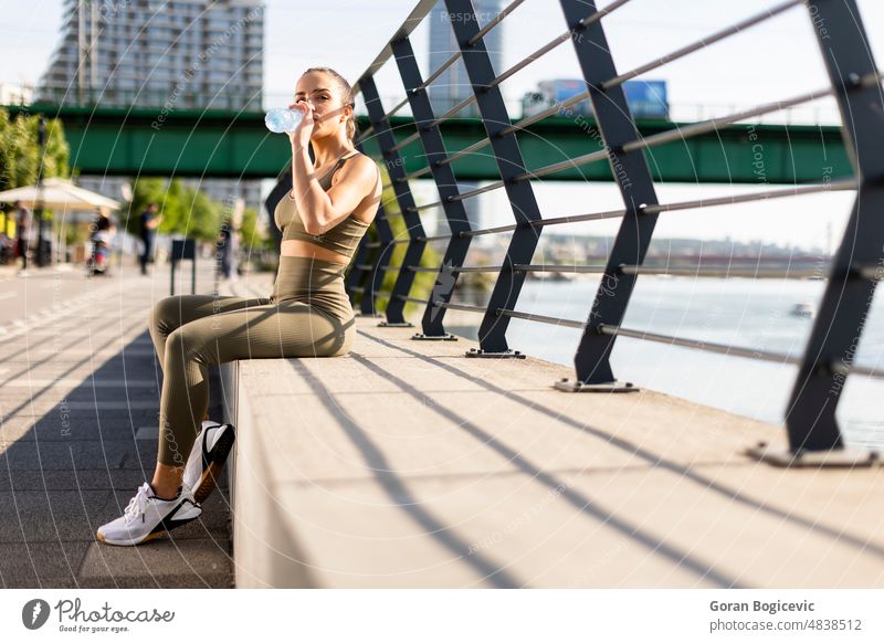 Hübsche junge Frau mit Kopfhörern macht eine Pause nach dem Laufen im städtischen Bereich Athlet sportlich arabisch Übung passen Fitness Flasche trinken