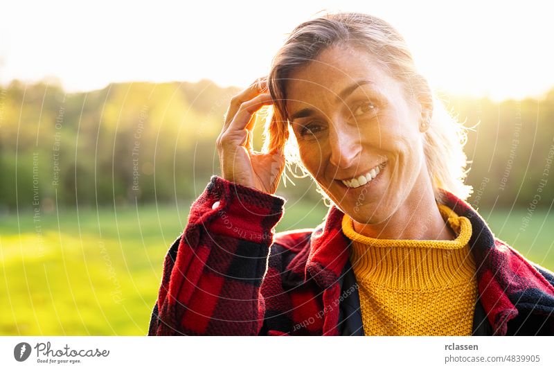 Porträt der schönen reifen Frau lächelnd und Blick weg im Park während des Sonnenuntergangs. Outdoor-Porträt eines lächelnden Mädchens. Glückliches fröhliches Mädchen lachend im Park mit kariertem Hemd.