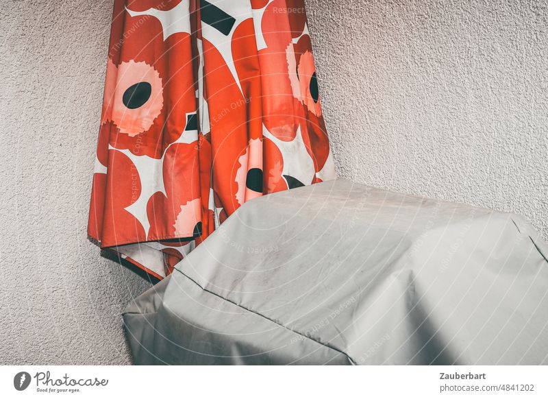 Sonnenschirm und abgedeckter Grill vor einer Wand Gasgrill rot Sommer Urlaub Erwartung verpackt eingepackt Verpackung Abdeckung verhüllt verborgen aufspannen