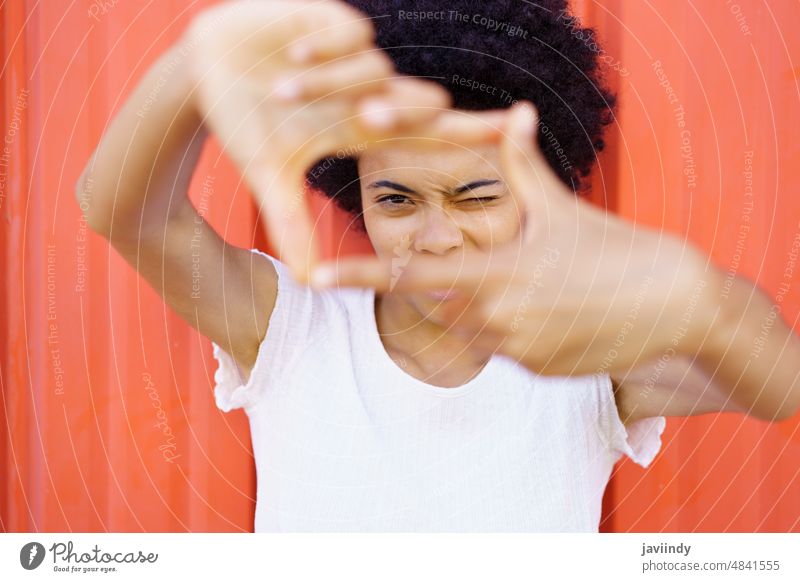 Fröhliche afroamerikanische Frau zeigt ein Bild aus den Händen wie ein Foto. Rahmen Zeichen Auge Gesicht gestikulieren schwarz lockig Person Mädchen im Freien