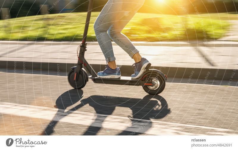 Frau fährt schwarzen elektrischen Kick-Scooter in Stadtlandschaft im Sommer, Bewegungsunschärfe Tretroller Großstadt E-Roller Stadtzentrum Turnschuh Fahrrad