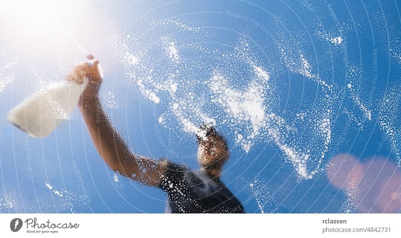 Mann reinigt Glasscheibe mit Sprühflasche - Frühjahrsputzkonzept Fenster Dienst Waschen Rakel Spray Flasche Waschmaschine baden blau Business Pflege