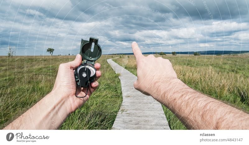 POV-Bild eines Reisenden, der einen Kompass hält und die Richtung in der Landschaft angibt. Mann Beteiligung pov Orientierung Hand Menschen Lifestyle