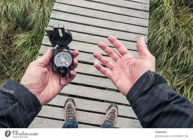 Mann hält einen Kompass und sucht die Richtung auf einer hölzernen Promenade, Sichtweise. Beteiligung pov Orientierung Hand Menschen Lifestyle Orientierungslauf