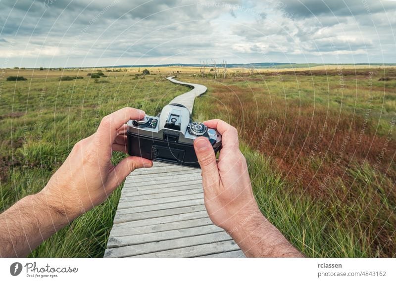 männliche Hand hält eine Vintage-Kamera gegen die eine Landschaft mit Promenade, um ein Bild zu nehmen, pov, Point of View Perspektive. Mann Beteiligung