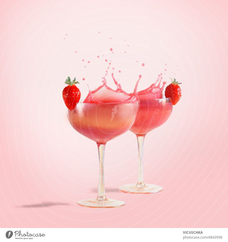Rosa Cocktail spritzt in Champagnergläser mit Erdbeeren auf rosa Hintergrund mit Sonnenlicht. Flüssigkeit in Bewegung. Geplätscher erdbeeren