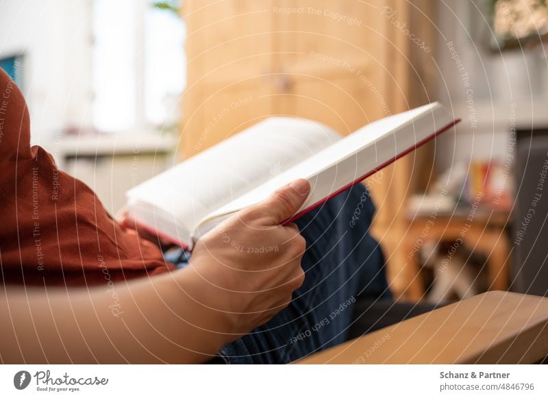 Person in einem Sessel liest gerade in einem Buch lesen Bücher gebunden entspannen Entspannung lernen Hand sitzen sessel Wohnung zuhause Ruhe Freizeit Roman