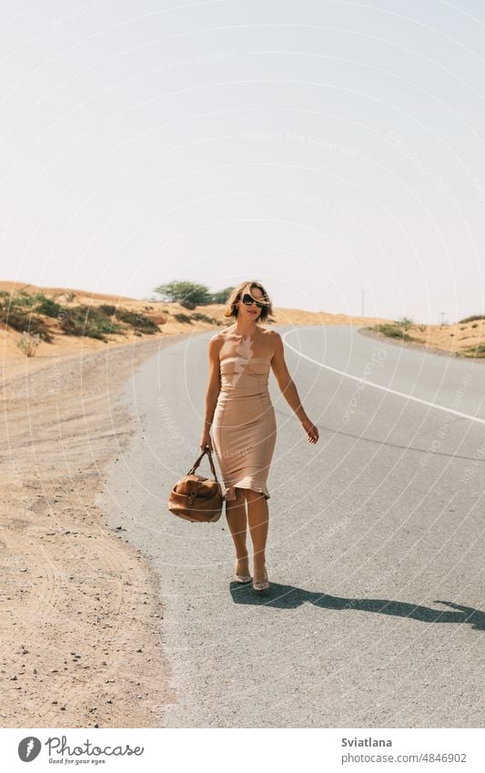 Ein glamouröses Mädchen in einem eleganten Kleid geht mit einer Tasche in der Hand eine verlassene Straße entlang. Glamour Stil schön Frau Porträt blond Mode