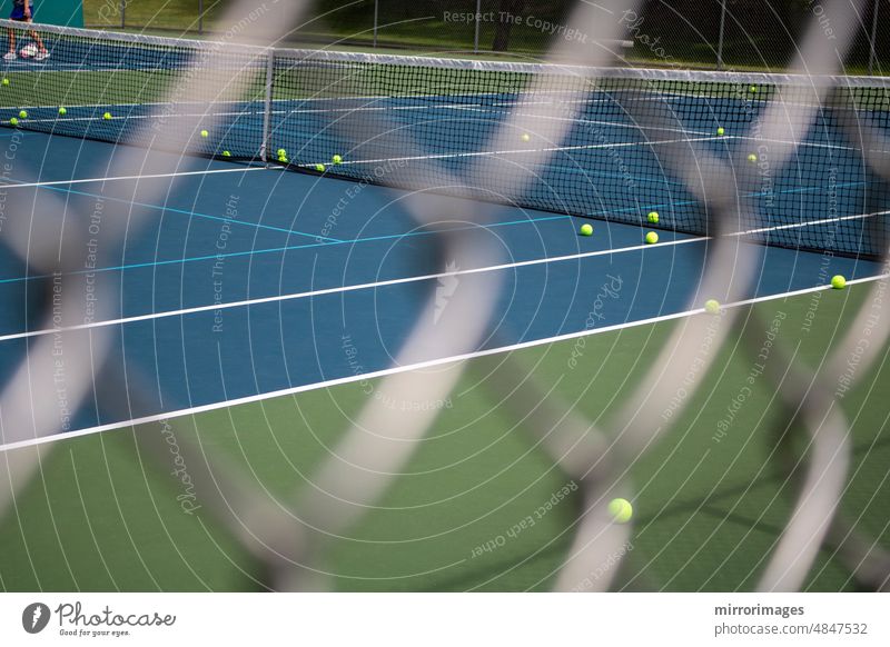 Tennisplatz durch einen verschwommenen rautenförmigen Zaun mit Bällen auf dem Spielfeld, die Beine einer Person in der Ferne Aktivität anketten