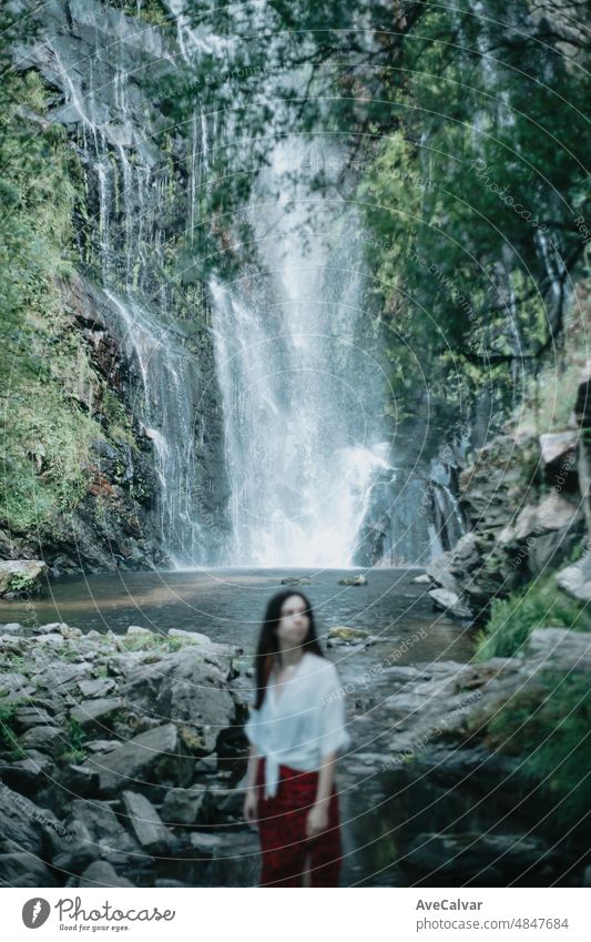 Unscharfes Frontalporträt junge Frau ruht und schaut einen Wasserfall, Meditation, Yoga und Denken Konzepte. Freiheit in der Natur, unabhängigen Lebensstil und Freiheit Konzept. Selektiver Fokus.