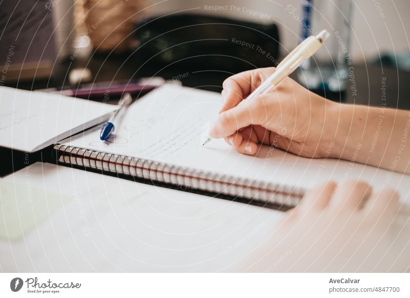 Nahaufnahme einer Frau, die mit der Hand auf ein Notizbuch schreibt, Hausaufgaben während der Universität macht, sich mit einem Lehrbuch auf eine Prüfung vorbereitet und Notizen macht, selektiver Fokus auf den Bleistift.