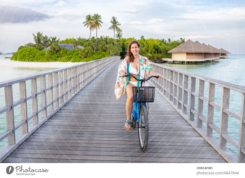 Frau mittleren Alters auf einem Fahrrad beim Überqueren einer Brücke auf einer maledivischen Insel asiatisch attraktiv Strand Küste Küstenlinie exotisch