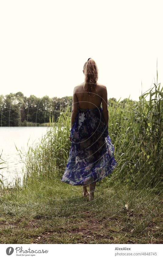 Junge, rotblonde, langhaarige Frau steht mit dem Rücken zur Kamera an einem See mit Schilf jung schön schlank draussen Gras Natur fröhlich glücklich natürlich