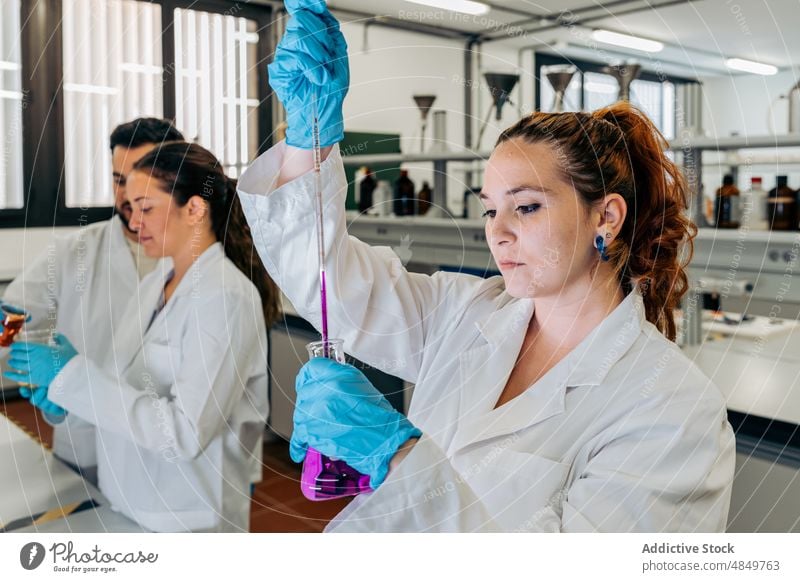 Chemiker gießt Flüssigkeit in Kolben im Labor Frau Wissenschaftler Chemikalie liquide eingießen Experiment Flasche Probe forschen Kompetenz Apotheke Kollege
