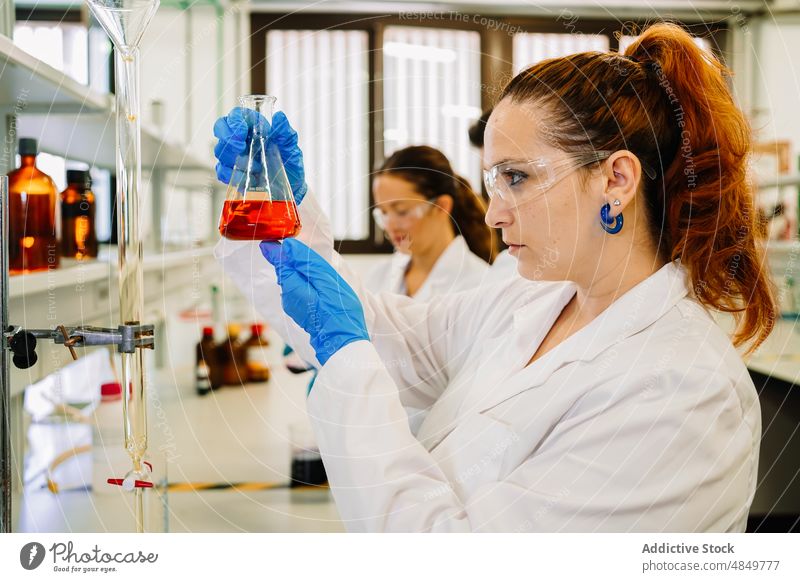 Seriöser Chemiker, der eine Flüssigkeit in einem Kolben im Labor untersucht Frau Wissenschaftler Flasche liquide untersuchen wissenschaftlich Chemikalie