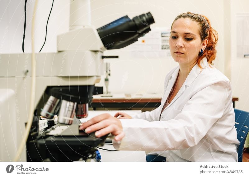 Chemiker, der eine Probe in das Mikroskop im Labor legt Frau Wissenschaftler Experiment forschen analysieren Chemie Kompetenz wissenschaftlich Fokus Arbeit
