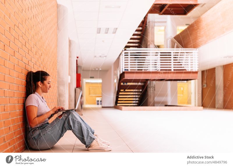 Fokussierte Frau, die in der Nähe einer Mauer auf ihrem Laptop surft Schüler Internet Browsen online Universität feiern Backsteinwand Netbook lernen Anschluss