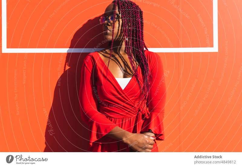 Seriöse junge schwarze Frau in trendigem Outfit Afrikanisch Porträt trendy Stil Afroamerikaner rot Wand sonnig ernst modern selbstbewusst Mode urban Frisur Zopf