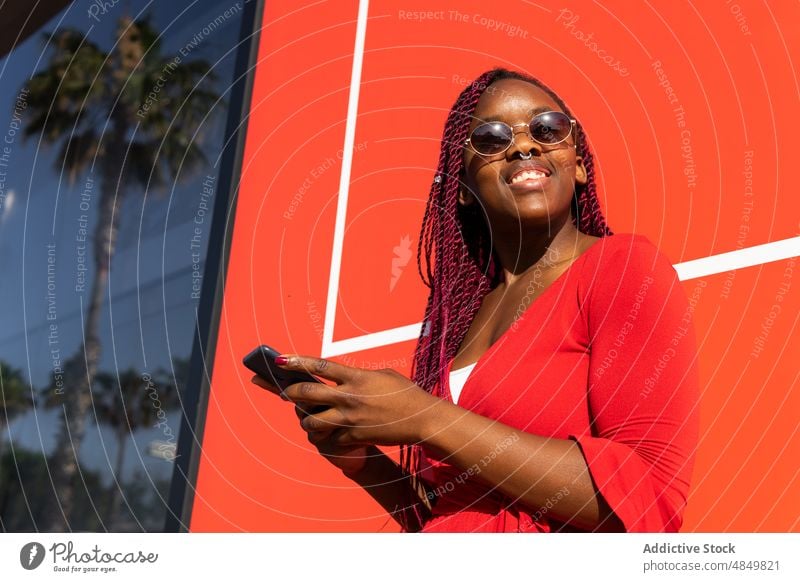 Fröhliche schwarze Frau mit Smartphone Afroamerikaner Straße Glück Mobile Lächeln heiter benutzend trendy Stil Telefon Großstadt Apparatur Gerät urban