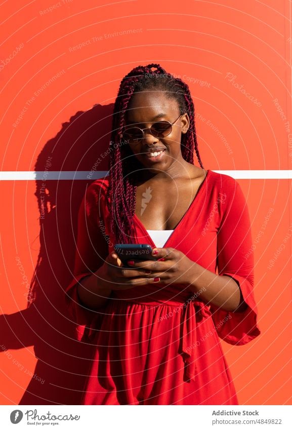 Fröhliche schwarze Frau mit Smartphone Afroamerikaner Straße Glück Mobile Lächeln heiter benutzend trendy Stil Telefon Großstadt Apparatur Gerät urban