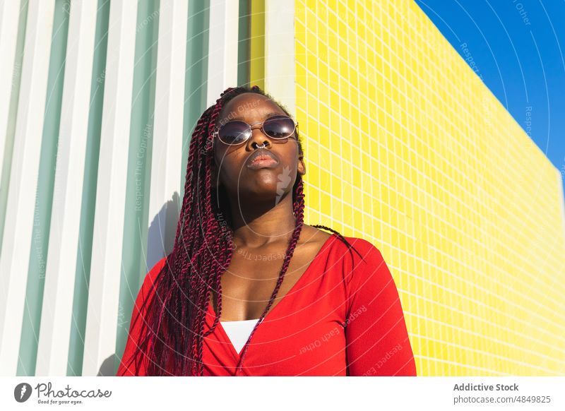 Schwarze Frau in trendigem Outfit und Sonnenbrille Porträt Lehnen Stil trendy Afroamerikaner Frisur sonnig modern selbstbewusst Mode rot urban