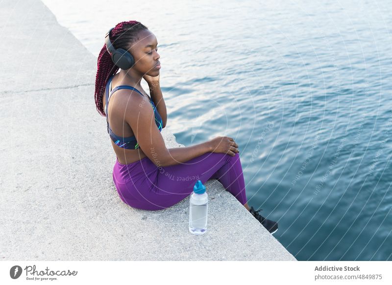 Entspannte schwarze Frau beim Musikhören Kopfhörer zuhören Konzentration Training Sportlerin Fitness Athlet Drahtlos passen Gerät Großstadt Apparatur im Freien
