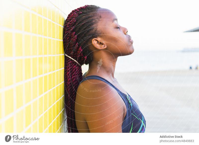Schwarze Sportlerin, die sich auf der Straße ausruht sich[Akk] entspannen Training passen geschlossene Augen Frau Lehnen Wand Fitness Athlet Sportbekleidung