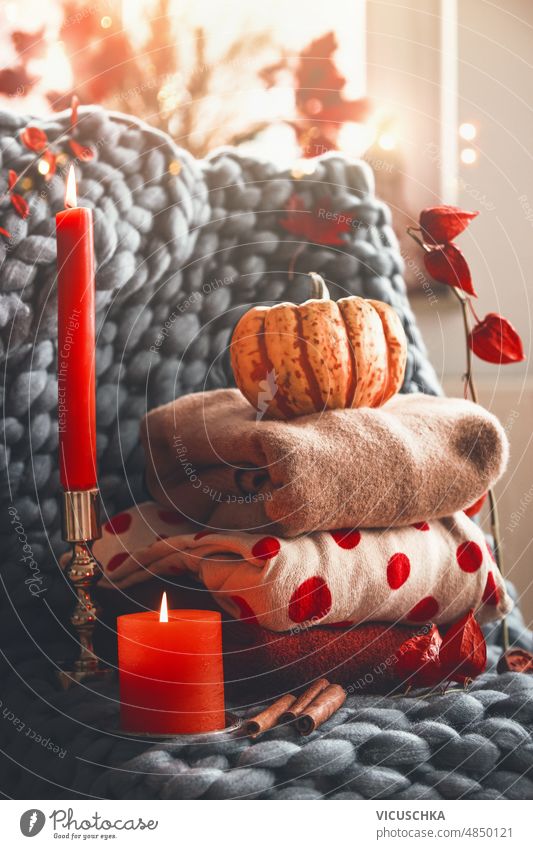 Gemütliches Herbststillleben mit gestrickten Wollpullovern, Kerze, Kürbis und Zweigen auf grauer Decke. gemütlich Stillleben Pullover Niederlassungen geheftet
