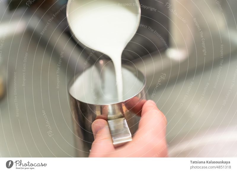 Ein Barista gießt aufgeschlagene Milch aus einer Stahlkanne in eine andere melken gedämpfte Milch Sahne Krug Kannen rostfrei Speise Gerichte Utensil Container