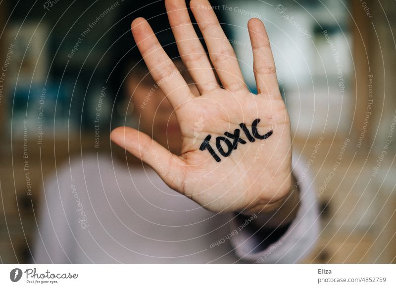 Frau hält ihre Hand, auf der Toxic geschrieben steht, in die kamera toxisch missbräuchlich negativ Verhaltensweise toxische Männlichkeit Manipulation Unangenehm