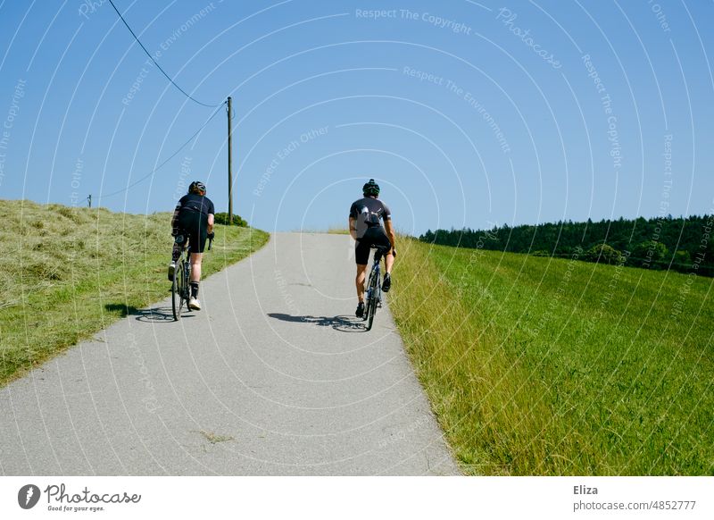 Zwei sportliche Fahrradfahrende bei einer Fahrradtour im Grünen Fahrradfahrerin Radsport grün Hügel bergauf Sommer Sonnenschein Außenaufnahme Sport Straße