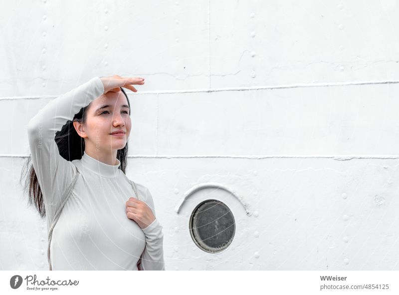 Eine junge Frau in Weiß vor einer Schiffswand schaut zuversichtlich in die Zukunft oder auch nur in die Ferne Mädchen Blick maritim Marine weiß beige hell