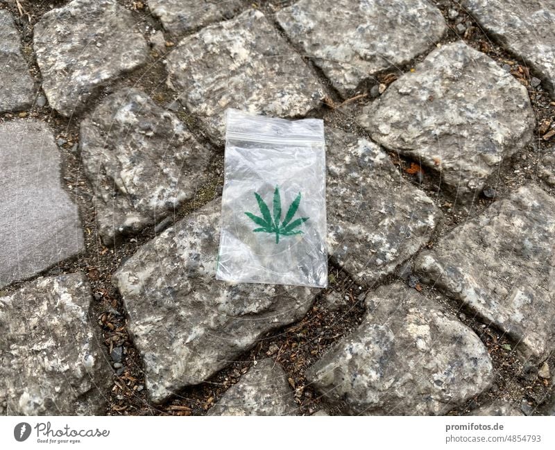 Kleines und leeres Plastiktütchen mit grüner Abbildung eines Hanfblattes auf dem Boden. Foto: Alexander Hauk tag tageslicht plastik tüte plastiktüte transparent
