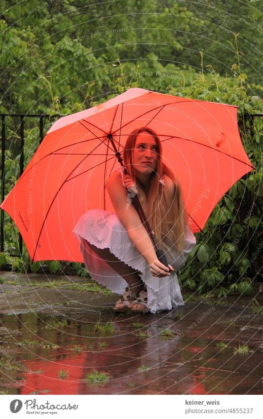 Eine langhaarige blonde Frau duckt sich unter rotem Regenschirm bei Regenwetter Schirm Wetter schlechtes Wetter Regenschutz nass Wasser Wassertropfen