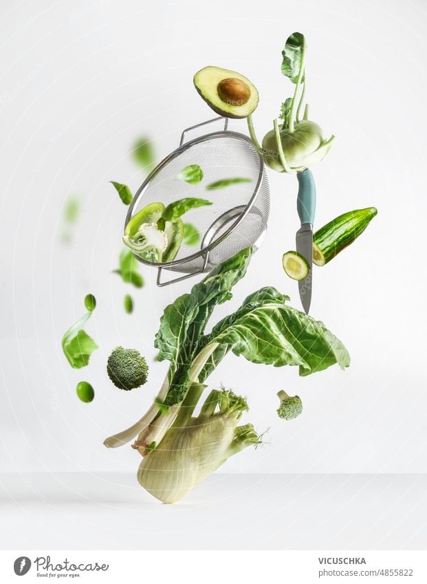 Balancing fliegenden grünen Gemüse Zutaten: Pak Choi, Avocado, Fenchel, Paprika Brokkoli, Edamame, Rübe Kohl mit Sieb und Küchenmesser auf weißem Hintergrund.