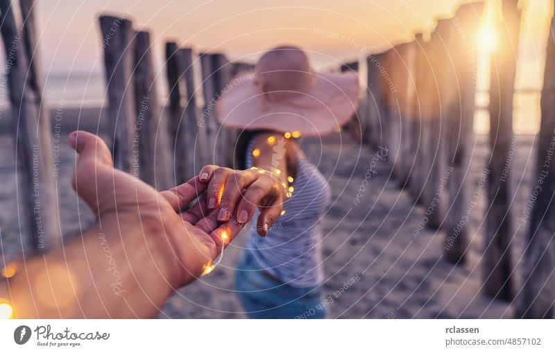 Paar, das sich an den Händen hält und bei Sonnenuntergang am Strand spazieren geht, Frau mit weißem Hemd und kurzen Jeans Hand Sommer Beteiligung reisen MEER