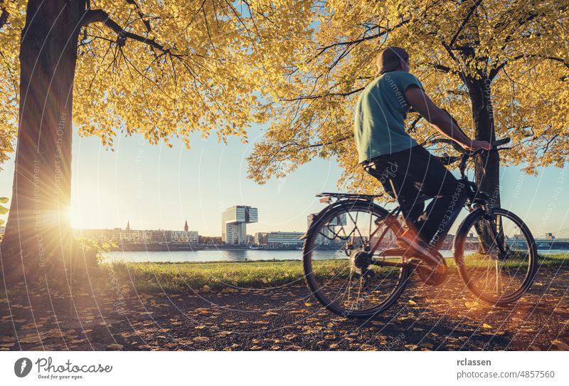 junger mann fährt mit dem fahrrad am rheinufer in köln, deutschland Köln Kranhäuser Vorabend Großstadt dom rheinauhafen Architektur Kölner Dom Ufer Sonne Wolken