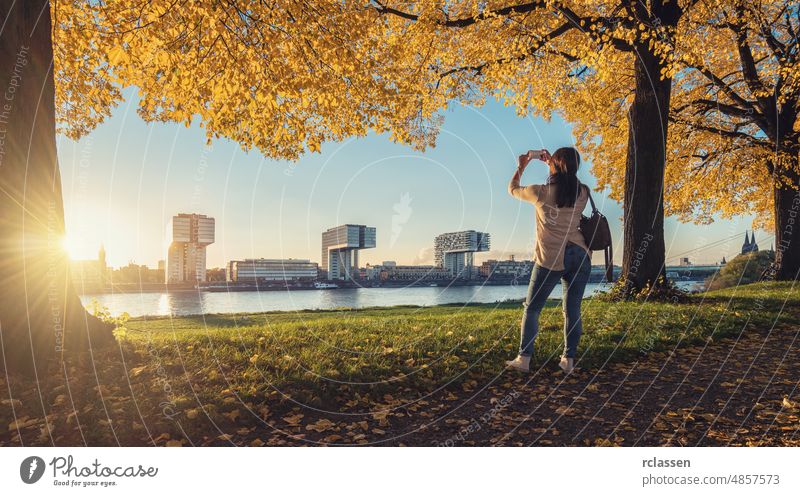 Frau macht ein Foto von der Skyline von Köln im Herbst Kranhäuser Vorabend Großstadt dom rheinauhafen Architektur Kölner Dom Ufer Sonne Wolken Himmel