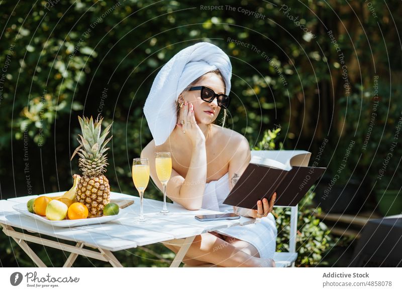 Frau in Handtüchern liest Buch auf Terrasse Handtuch Morgen patio lesen Literatur Leseratte Hobby Zeitvertreib Freizeit Saft Getränk trinken feminin Sommer Glas