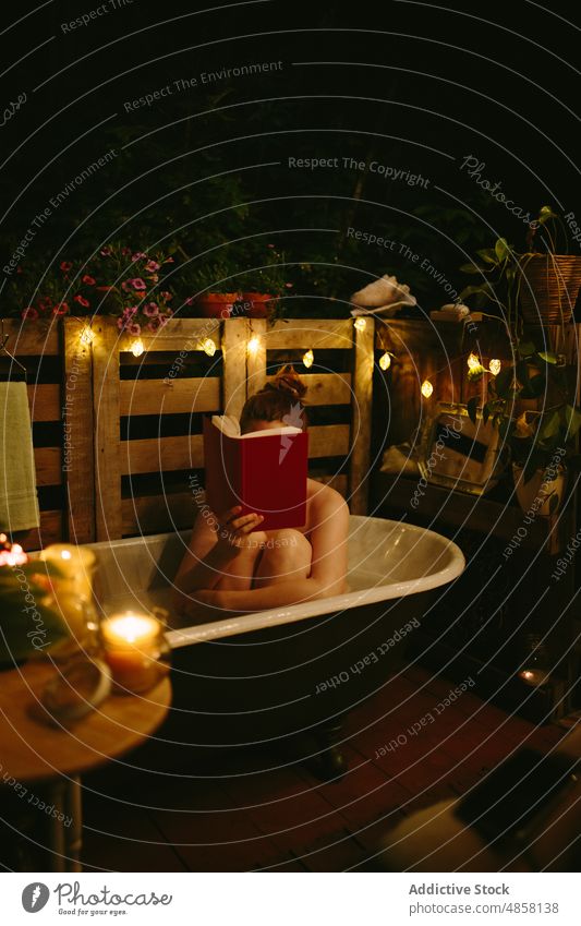 Gesichtslose Frau liest ein Buch in der Badewanne auf der Terrasse Abend patio Hobby Zeitvertreib nackt lesen Deckblatt glühen Girlande Literatur glänzend