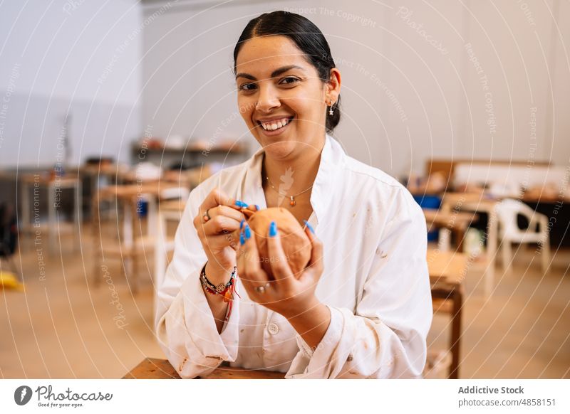 Glückliche hispanische Frau schnitzt Ornament auf Ton Kunstgewerbler Töpferwaren schnitzen Lächeln kreativ Hobby Basteln Porträt Tisch Werkstatt professionell