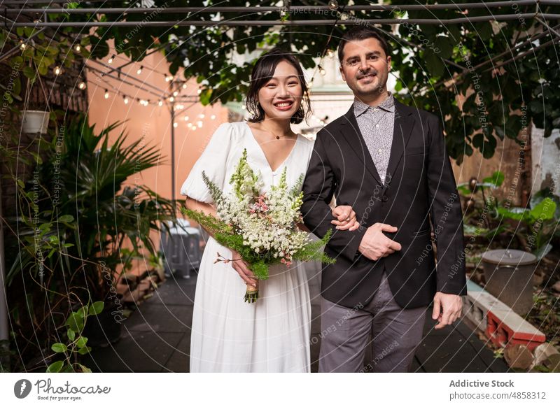 Glückliche diverse Jungvermählte mit Blumenstrauß im Garten Jungvermählter Paar Liebe Hochzeit feiern Heirat verliebt Zusammensein Braut striegeln romantisch