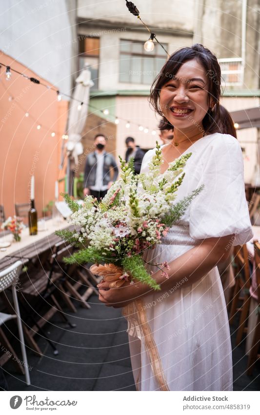 Junge ethnische Braut mit Blumenstrauß Frau Hochzeit Lächeln feiern Heirat Straße Verlobte asiatisch Blütezeit Zahnfarbenes Lächeln Glück heiter Freude positiv