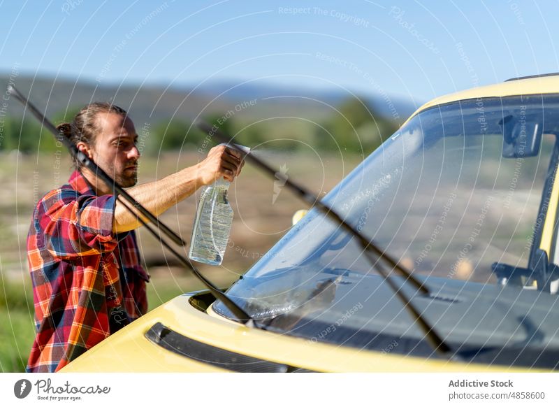 Männlicher Reisender, der die Windschutzscheibe seines Autos wäscht Mann Waschen Kleintransporter Landschaft Autoreise Spray Spülmittel Sauberkeit männlich