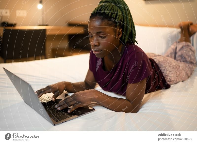 Schwarze Frau mit Laptop auf dem Bett Browsen Netbook Arbeit abgelegen Schlafzimmer freiberuflich online modern beschäftigt ethnisch schwarz Afroamerikaner